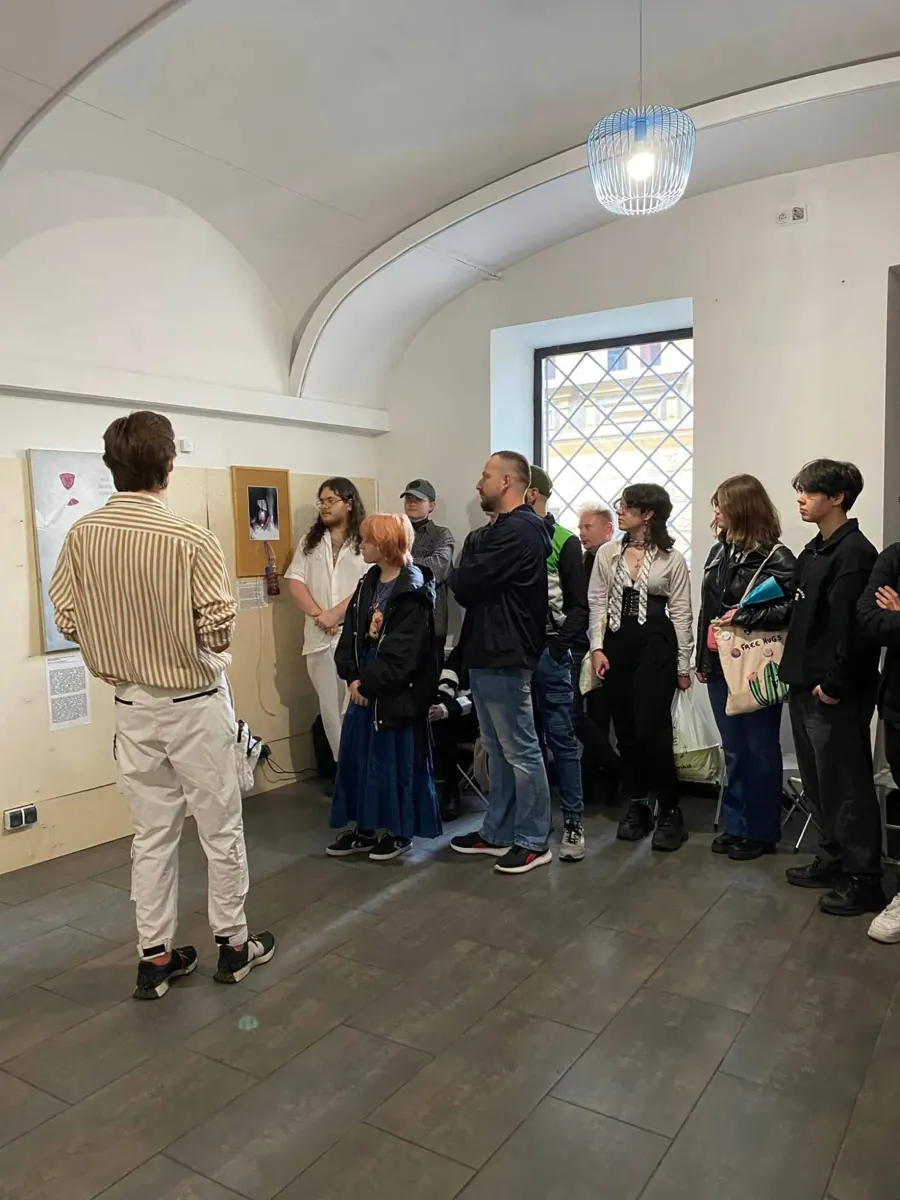 Artur Sendyka, seen from behind, talking to a group of people about paintings in a vaulted gallery room.