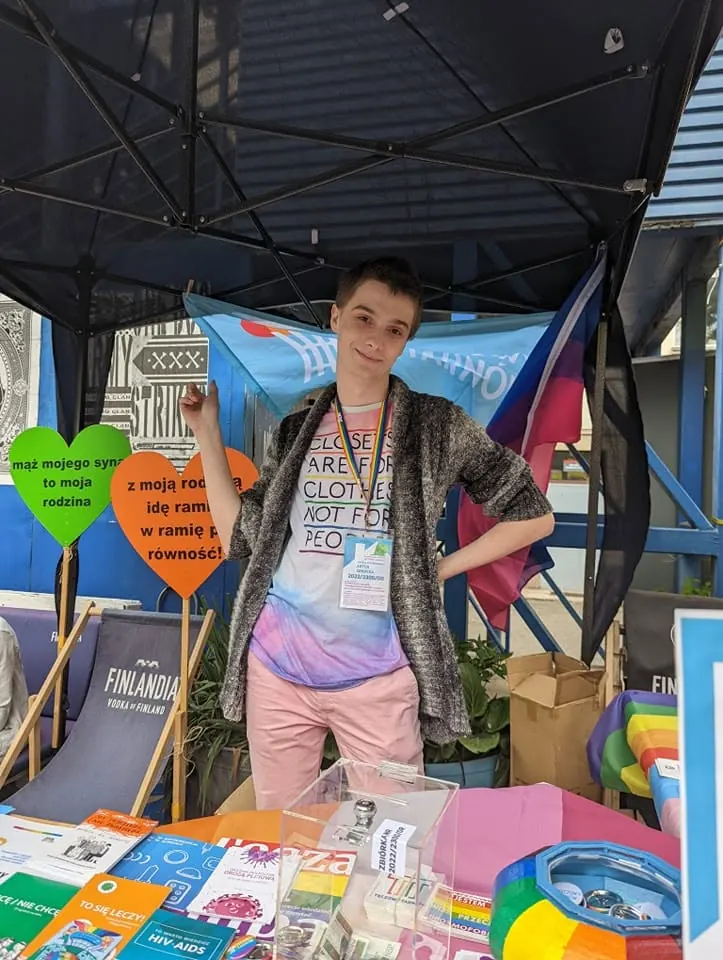 Artur Sendyka at a table with leaflets under a tent, next to paper hearts with equality slogans.